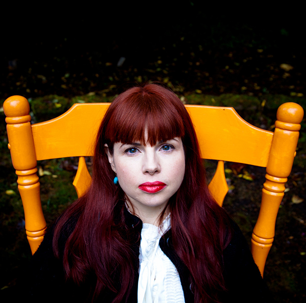 Kelly Sue DeConnick sitting in a yellow wooden chair